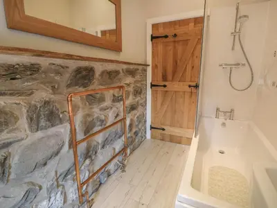 a bathroom with a stone wall and a bath tub at Tyn Ffynnon in Dyffryn