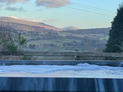 a hot tub with a view of a mountain at Peacock Cottage, Coity Bach in Talybont