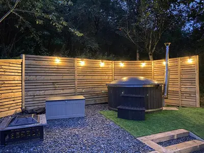 a privacy fence with a hot tub and lights on it at Woodland Pod in Corwen