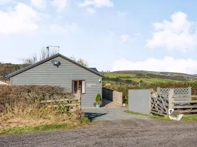a small house with a wooden gate and a fence at Cuckoo Hill Lodge in Saint Harmon