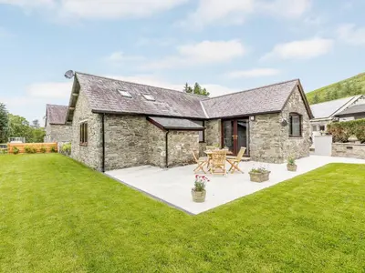 an exterior view of a stone house with a lawn at Cwm Dulas in Llanddewi-Brefi