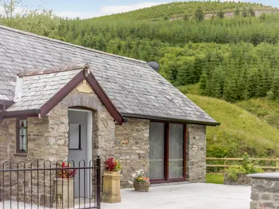 a stone house with a fence in front of a mountain at Cwm Dulas in Llanddewi-Brefi