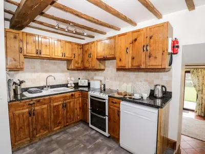 a kitchen with wooden cabinets and white appliances at Wilstone Cottage in Church Stretton