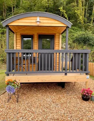 a large wooden gazebo in a yard with flowers at Shepherds Hut at Wern Mill in New Quay