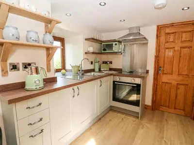 a kitchen with white cabinets and a wooden door at Tegfan Barn in Rhayader