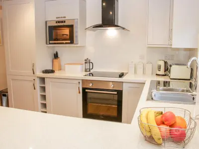 a kitchen with white cabinets and a basket of fruit at Conkers' Cottage in Church Stretton