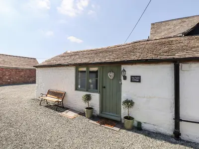 a white building with a green door and a bench at Top Farm Cottage in Oswestry