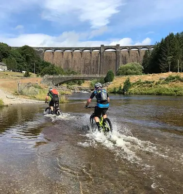 two people riding bikes in the water in a river at Gwilym's Stable in Builth Wells