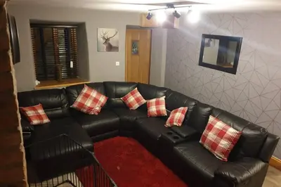 a black leather couch with four red and white pillows at Cosy Minffordd Let - Llanuwchllyn near, Bala LL23 in Bala
