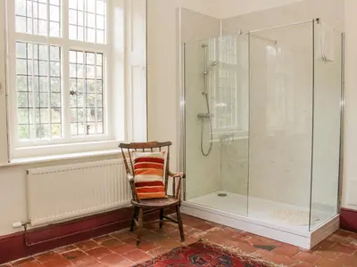 a bathroom with a shower and a wooden chair at The Generals Quarters at Pitchford Estate in Shrewsbury