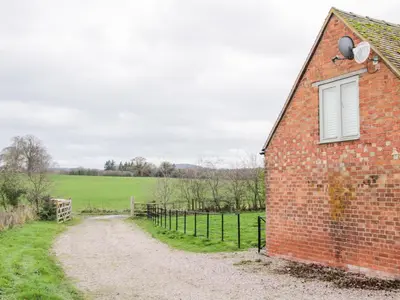 a brick building with a window and a dirt road at Treehouse Barn at Pitchford Estate in Shrewsbury