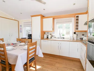 a kitchen with white cabinets and a table and chairs at McAuliffe Lodge in Borth