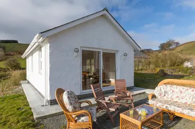 a small white cottage with chairs and a table at Merlin Cottages in Llandovery
