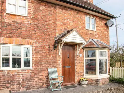 a brick house with a wooden door and a chair at 1 Royal Oak Cottages in Shrewsbury