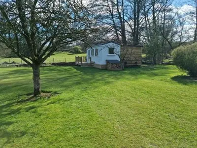 a small house in a field with a tree at Riverside Cabin - Sleeps 2 - HotTub - Parking in Oswestry