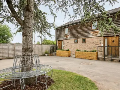 a metal bench next to a tree next to a building at Beekeeper's Cottage in Leominster