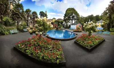two gardens with trees and flowers next to a swimming pool at Portmeirion Village & Castell Deudraeth in Porthmadog