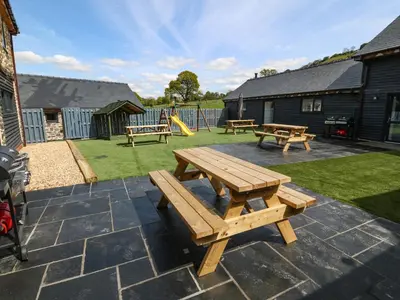 a patio with three picnic tables and a playground at Y Beudy The Dairy in Oswestry