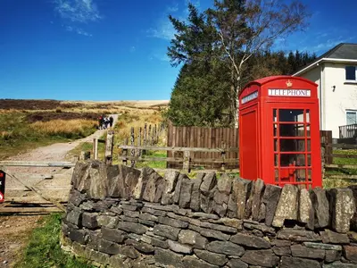 a red phone booth sitting next to a stone wall at Kooky Cottage in Brecon