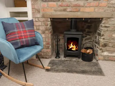 a chair in front of a brick fireplace with a stove at Kooky Cottage in Brecon
