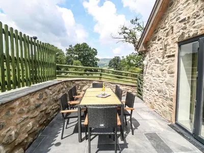 a table and chairs on a patio with a stone wall at Y Stabl The Stable in Oswestry