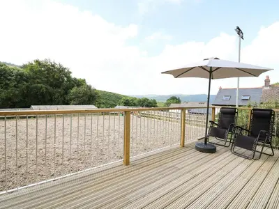 a deck with two chairs and an umbrella at Caban Glas in Aberystwyth