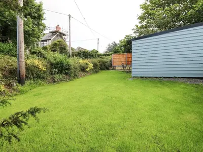a yard with a building and green grass at Caban Glas in Aberystwyth