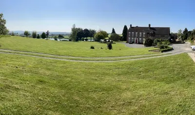 a large grassy field with a house in the background at Winsley Park Farm in Leominster