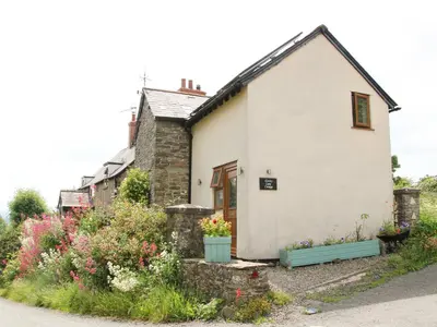 a white cottage with flowers in front of it at Linley Lane Cottage in Bishops Castle
