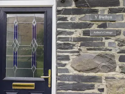 a door to a stone building with a sign on it at Arthurs Cottage in Tywyn