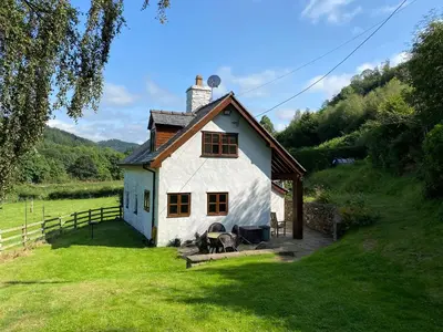 a small white house in a grassy field at Tan Y Garth Cottage in Corwen