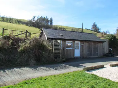 a small cabin with a white door in a field at Wild Valley Bunkhouse in Llanrhaeadr-ym-Mochnant