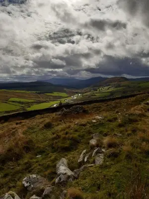 a view of a grassy hill with a cloudy sky at Penystryd in Trawsfynydd