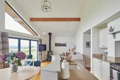 a kitchen and living room with white cabinets and a table at Lower Tumble Cottage in Llandyssil