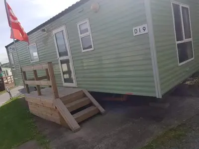a green mobile home with a bench and a flag at D19 in Aberystwyth