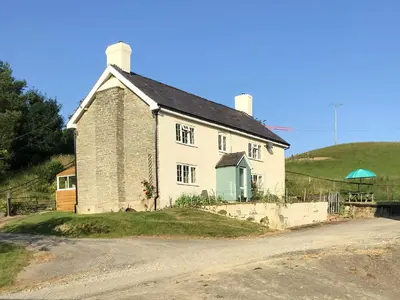 a white house on a hill next to a dirt road at Lower Farm in Llanfihangel Rhydithon