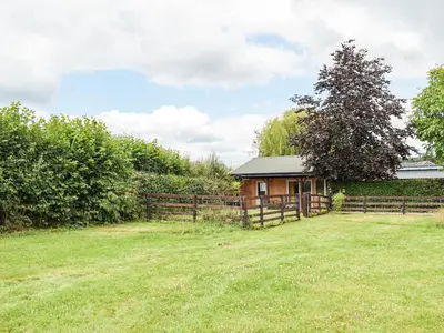 a house in a field next to a fence at The Lodge At Forbury Cottage in Kimbolton