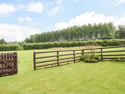 a wooden fence in a yard with a field at The Lodge At Forbury Cottage in Kimbolton