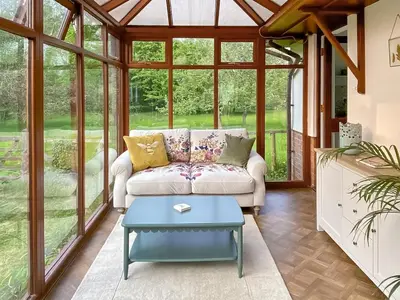 a conservatory with a couch and a table at Rose Cottage in Blakemere