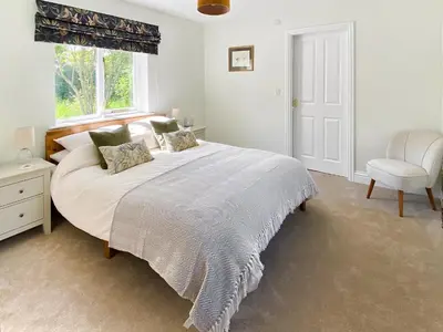 a bedroom with a large white bed and a chair at Rose Cottage in Blakemere