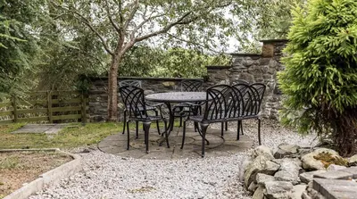a table and chairs in a garden with a stone wall at Stunning Barn Conversion with HOT TUB and ALPACAS - Ty Cerrig Barn in Corwen