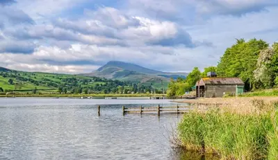 a lake with a barn and mountains in the background at Romantic Couples' Getaway - at Ty Cerrig Barn with luxury hot tub in Corwen
