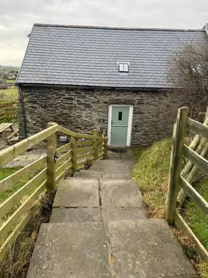 a stone building with a white door and a fence at Barn Retreat with Valley Views & Onsite Dog Field in Bryn-crug