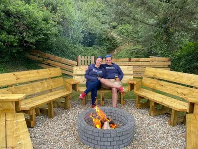 a man and a woman sitting on benches next to a fire at Farmhouse with Log Fire & On-Site Dog Field in Bryn-crug