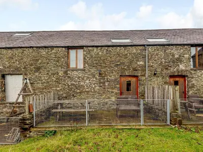 an old stone house with a fence in front of it at Robins Nest - Uk36208 in Llanfihangel-y-creuddyn
