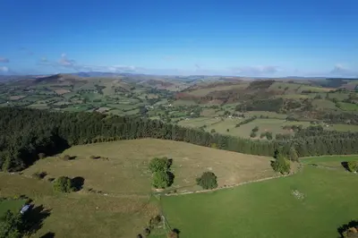 an aerial view of a green field with trees at The Nook at Pentregaer Ucha, with tennis court & lake. in Oswestry