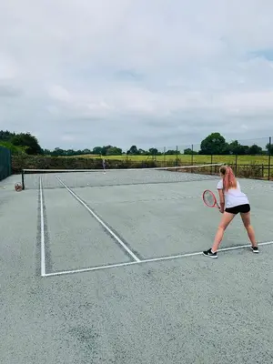 a woman playing tennis on a tennis court at The Nook at Pentregaer Ucha, with tennis court & lake. in Oswestry