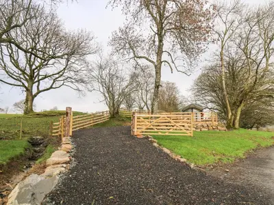 a wooden fence next to a field with trees at Woodland Escape in Rhayader