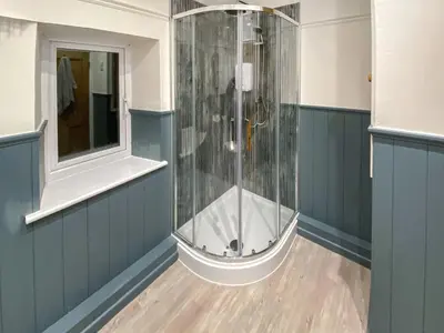 a shower in a bathroom with blue walls and wooden floors at New Cottage in Penmaenpool