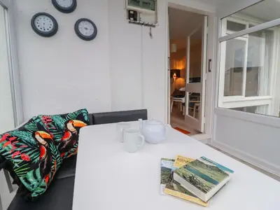 a white table with a book and clocks on the wall at 48 Glan Y Mor in Fairbourne